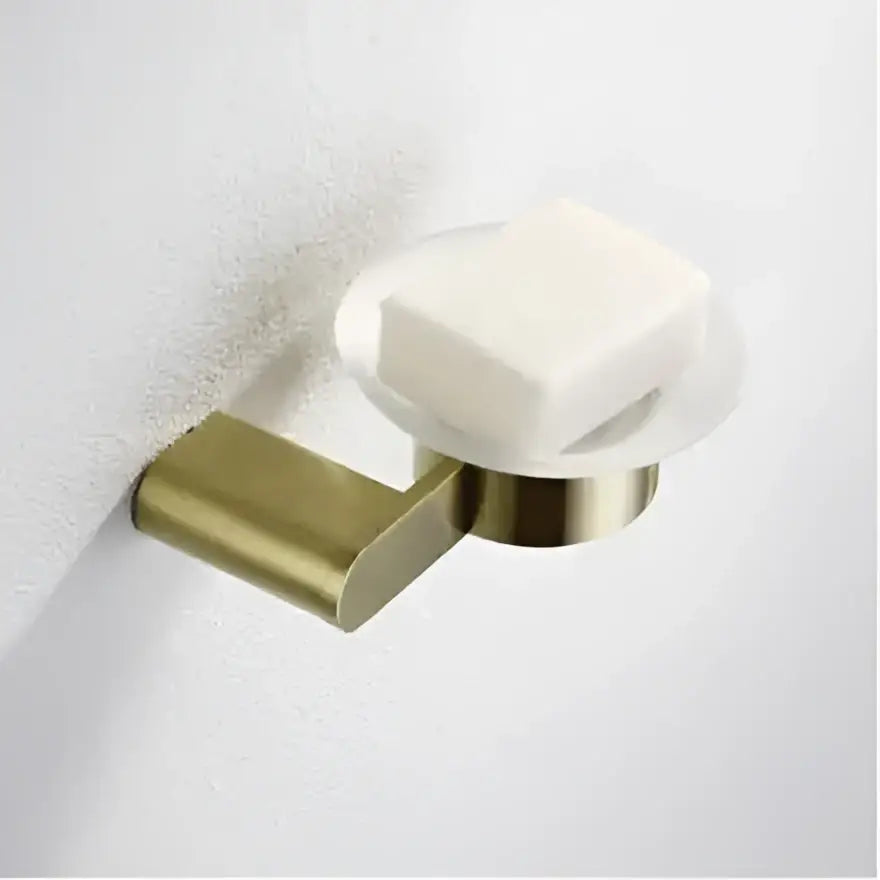 Brass-finished wall-mounted soap dish with clear glass top holding white soap in decorbites brushed gold hardware set