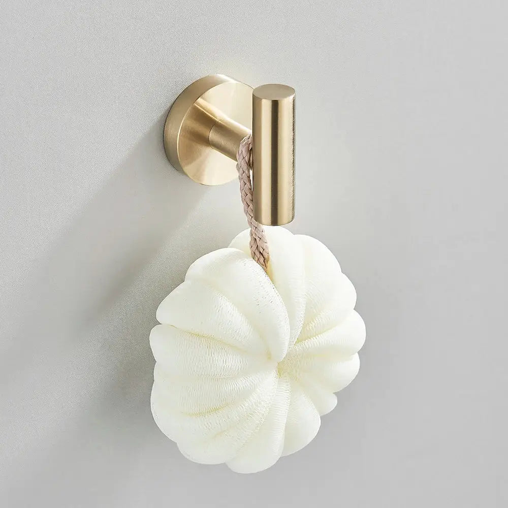 A white flower-shaped loofah with braided rope hangs from a decorbites brushed gold hardware set hook in a brushed gold bathroom
