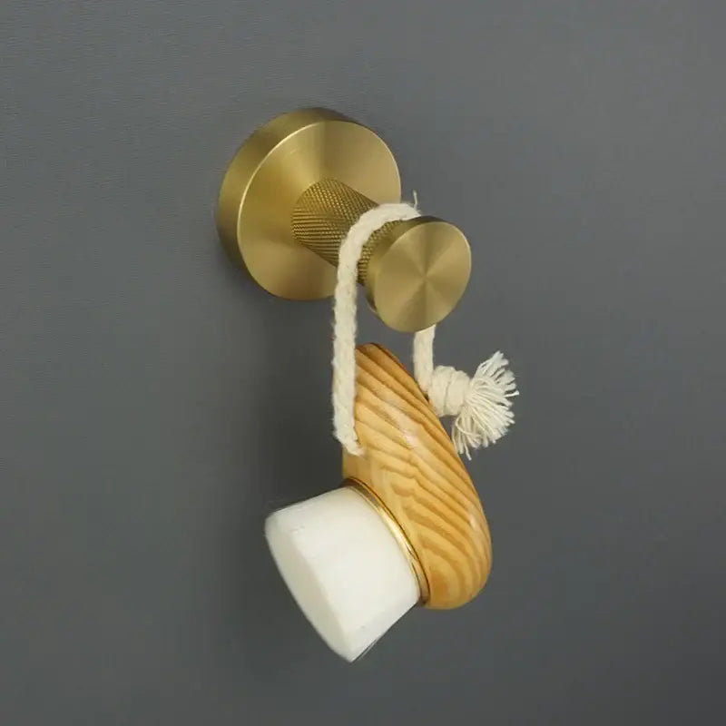 A wooden and white ceramic soap dish with a brushed gold metal rim hanging from a brass hook in a brushed gold bathroom set