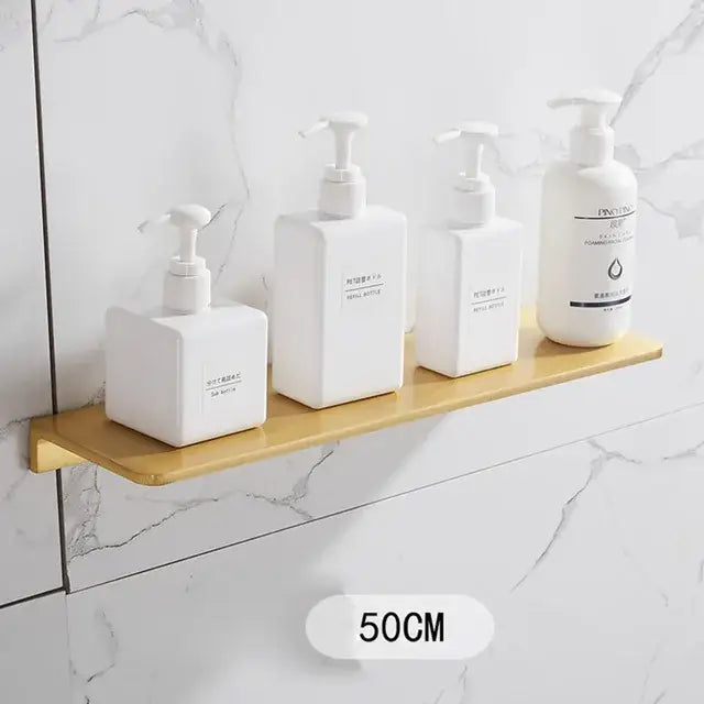 Modern brushed gold bathroom set with gold rectangular shelf holding four white pump bottles decorbites brushed gold
