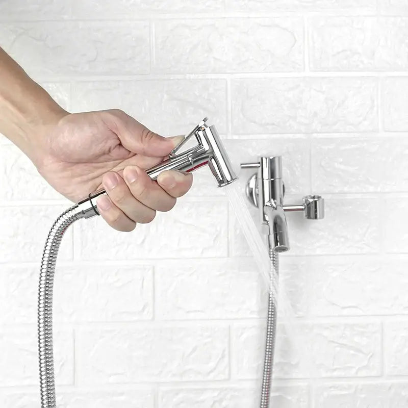 Shiny chrome handheld bidet sprayer with flexible metal hose attached to wall-mounted faucet in bidet faucet set