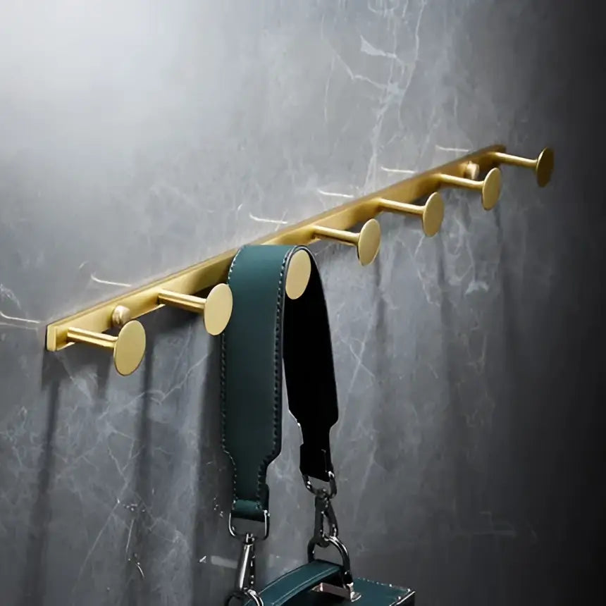 Modern brushed gold brass bath hardware set with six circular hooks mounted on wall holding dark green leather strap