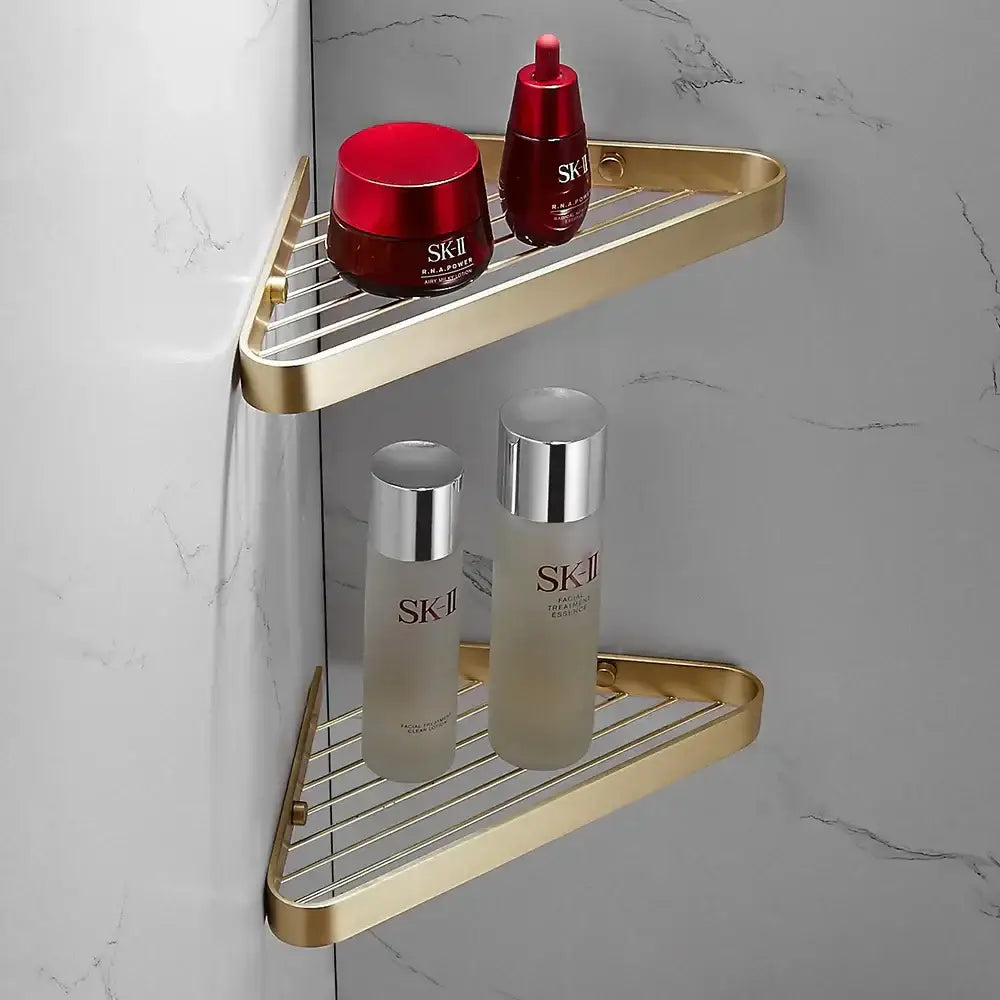 Modern brushed gold brass bath hardware set featuring a gold triangular wire mesh shelf holding sk-ii skincare products