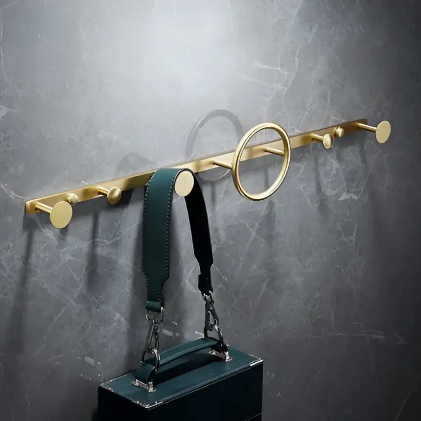 Modern brushed gold brass bath hardware set features a wall-mounted coat rack with round pegs holding a dark green handbag