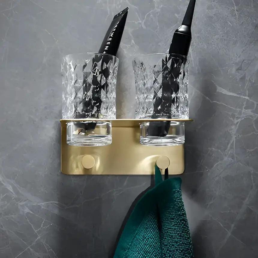 Modern brushed gold brass bath hardware set featuring a wall-mounted toothbrush holder with faceted crystal cups holding black toothbrushes