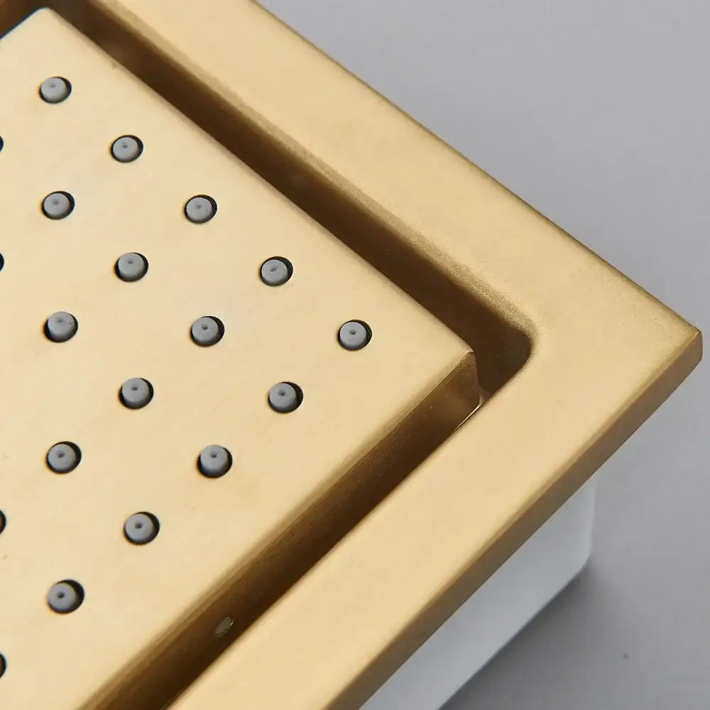 Gold-colored square shower drain with brushed metallic finish and circular holes for modern brushed gold shower head systems