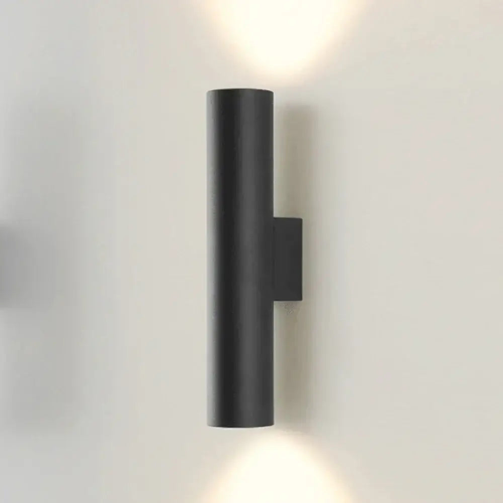 Modern brushed gold and matte black cylindrical wall lamp with minimalist design emitting warm light top and bottom