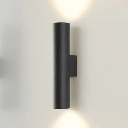 Modern brushed gold and matte black cylindrical wall lamp with minimalist design emitting warm light top and bottom