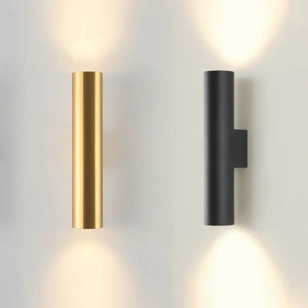 Modern brushed gold and matte black cylindrical wall lamps emitting a warm glow for bedroom lighting use