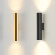 Modern brushed gold and matte black cylindrical wall lamps emitting a warm glow for bedroom lighting use