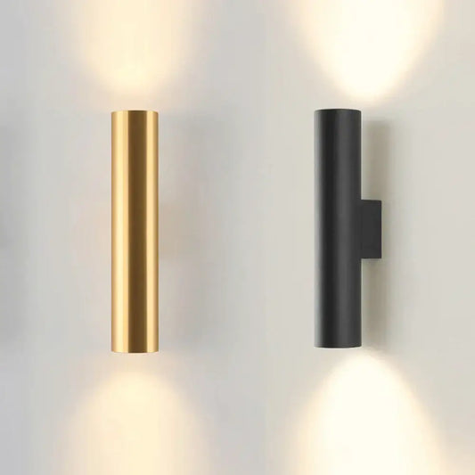 Modern brushed gold and matte black cylindrical wall lamps emitting a warm glow for bedroom lighting use
