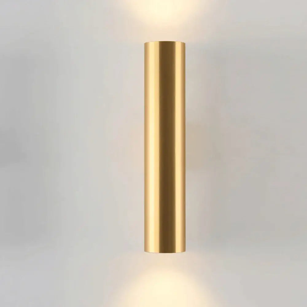 A sleek cylindrical wall lamp in brushed gold with matte black accents designed for modern bedroom lighting
