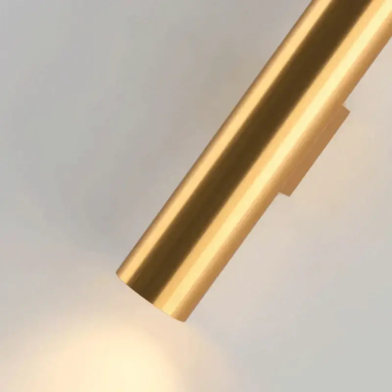 A sleek cylindrical brass wall lamp with polished finish and subtle horizontal grooves for modern bedroom lighting