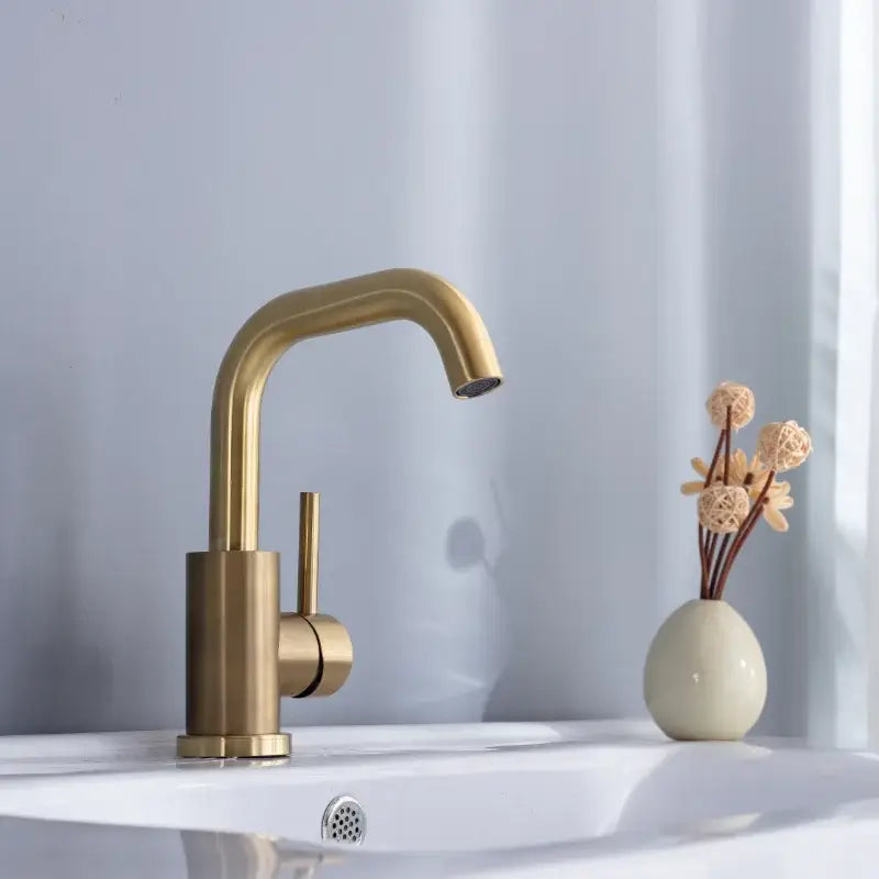 Modern brushed gold single handle basin faucet with sleek curved spout and cylindrical base for bathroom use