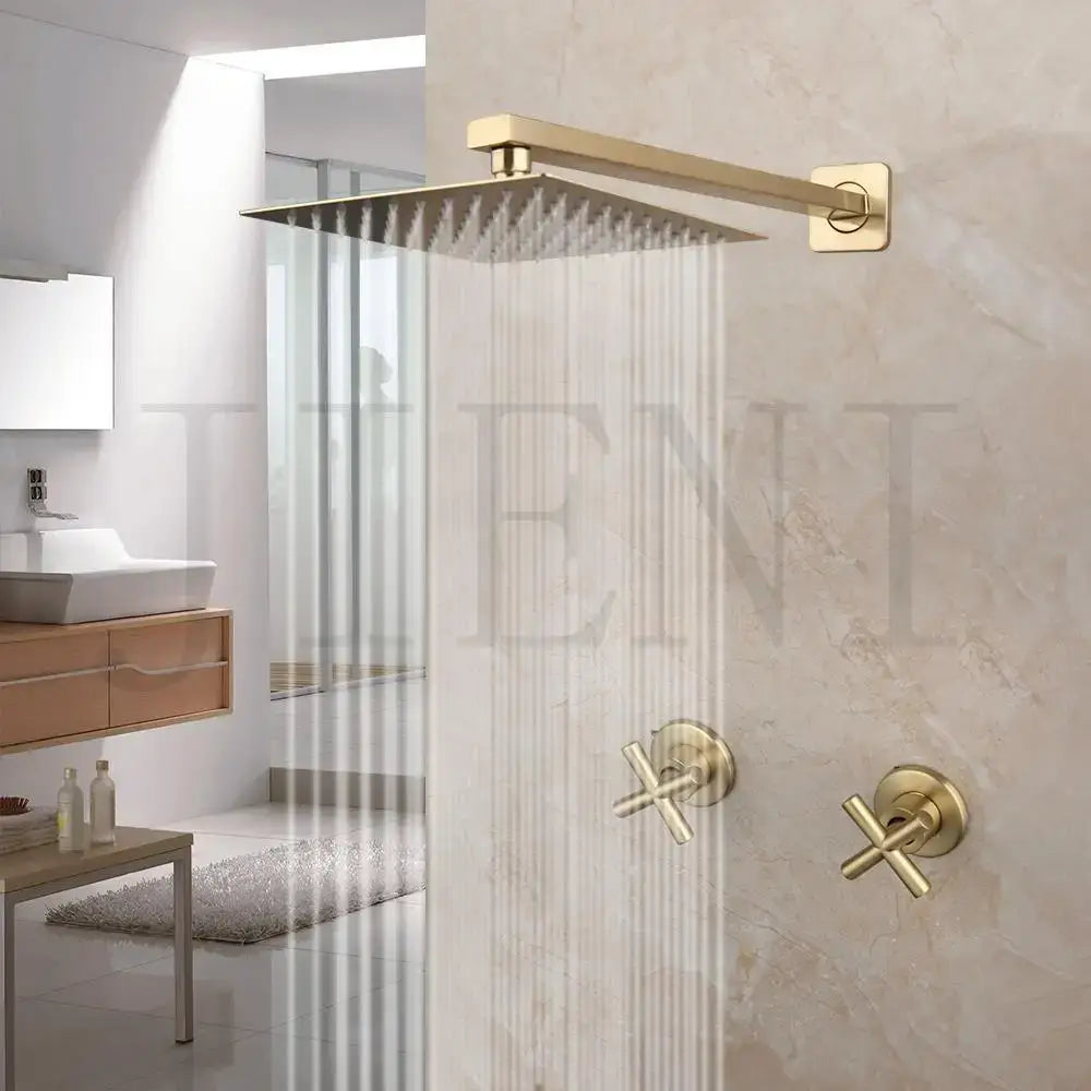Modern brushed gold square rainfall shower set with gold-toned rain shower head and cross-handle faucets on marble wall