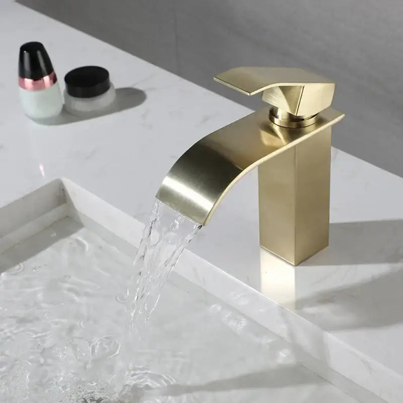 Modern brushed gold stainless steel basin faucet with a sleek rectangular waterfall spout and brushed metal finish