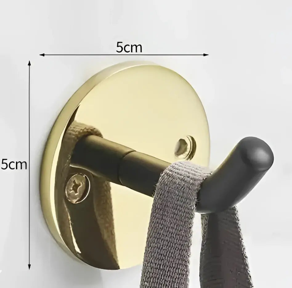 Modern brushed gold stainless steel robe hook with black curved arm holding gray knitted towel in bathroom