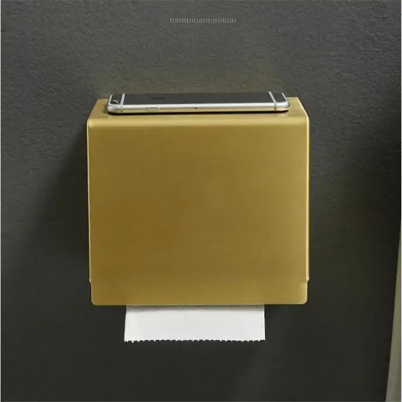 Modern brushed gold wall-mounted toilet paper holder with sleek rectangular design and a silver smartphone on top