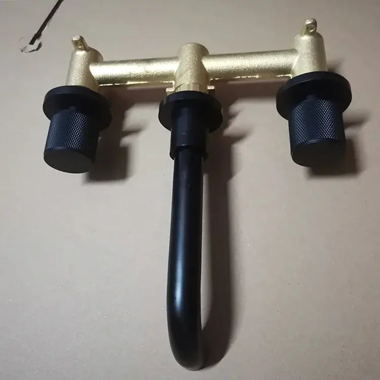 Modern brushed gold wall mount faucet with black textured handles and a curved spout for bathroom use