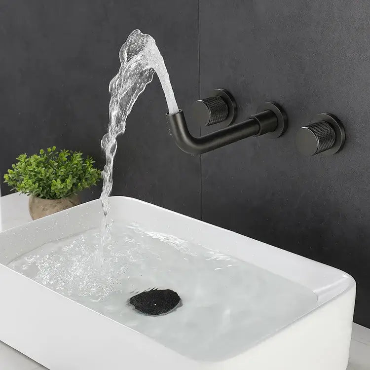 Modern brushed gold wall mount faucet with textured handles and curved spout pouring water into white rectangular sink