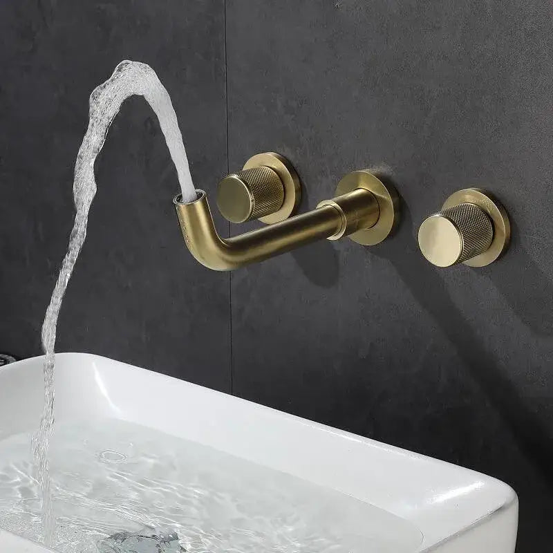 Modern brushed gold wall mount faucet with textured knobs and curved spout flowing water into white sink