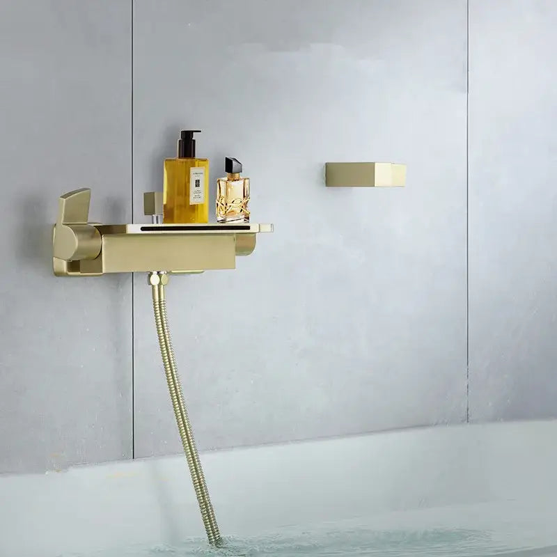 Modern brushed gold waterfall shower faucet set featuring a gold-finished bathtub faucet with integrated shelf holding perfume bottles