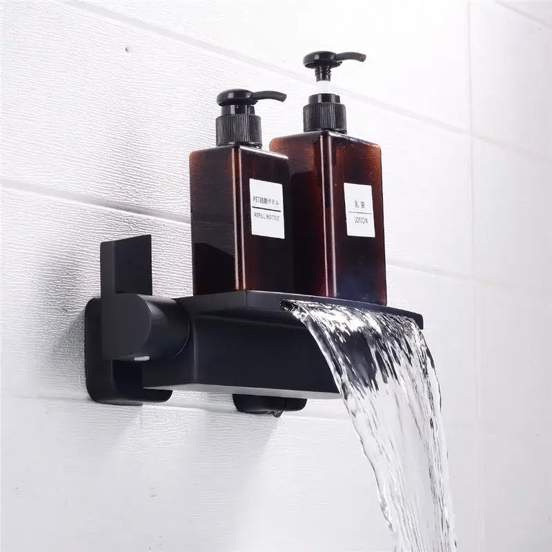 Black wall-mounted shower caddy with two amber pump bottles paired with modern brushed gold waterfall shower faucet set