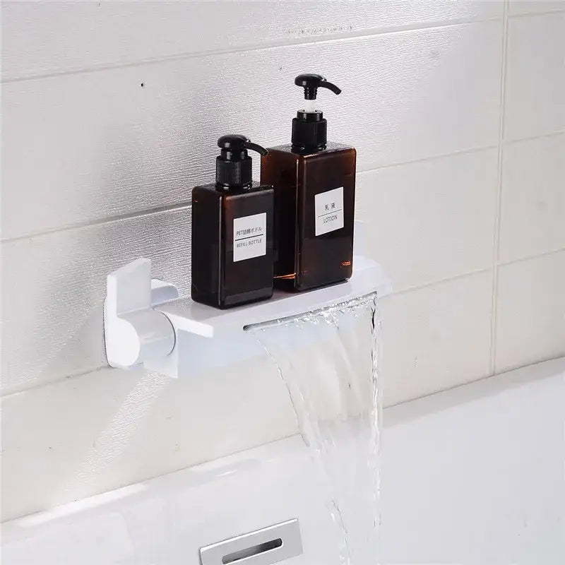 White wall-mounted soap dispenser shelf holding two dark brown pump bottles below a modern brushed gold shower faucet set