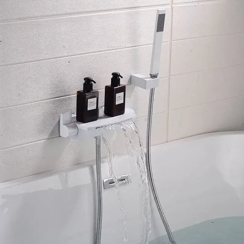 White wall-mounted shower shelf holding two black pump bottles beside modern brushed gold waterfall shower faucet set