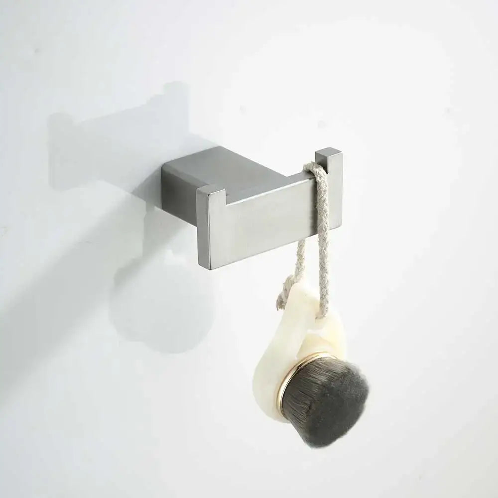 Silver rectangular wall-mounted hook holding cream bath brush with dark bristles in modern bathroom hardware set