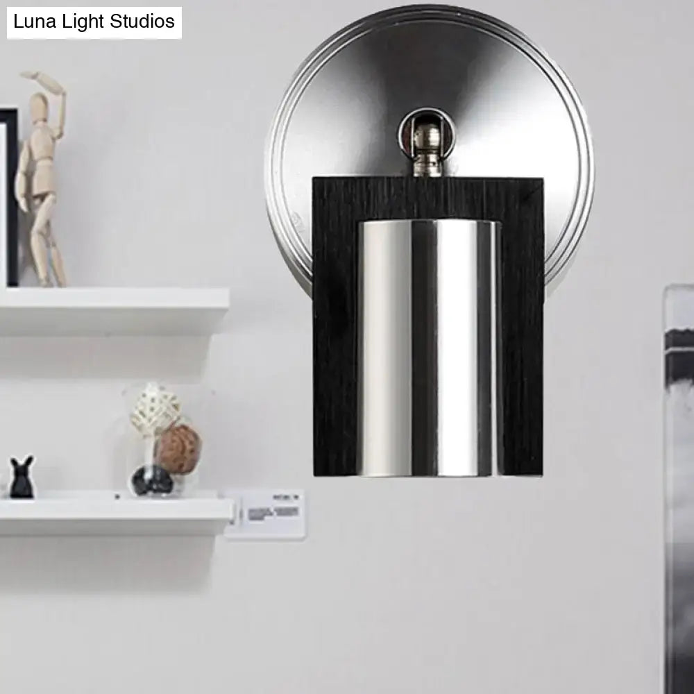 Modern brushed nickel wall sconce with metal shade and dark wood frame emitting warm white light for bedroom use