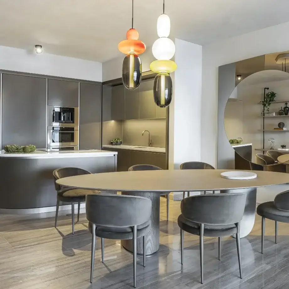 Modern oval dining table with light wood top and minimalist metal legs beneath decorbites candy glass ceiling chandelier