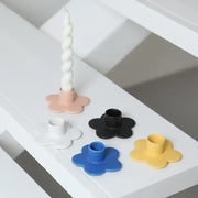 A set of five pastel and bold cartoon flower candle holders in matte plastic with one holding a white taper candle