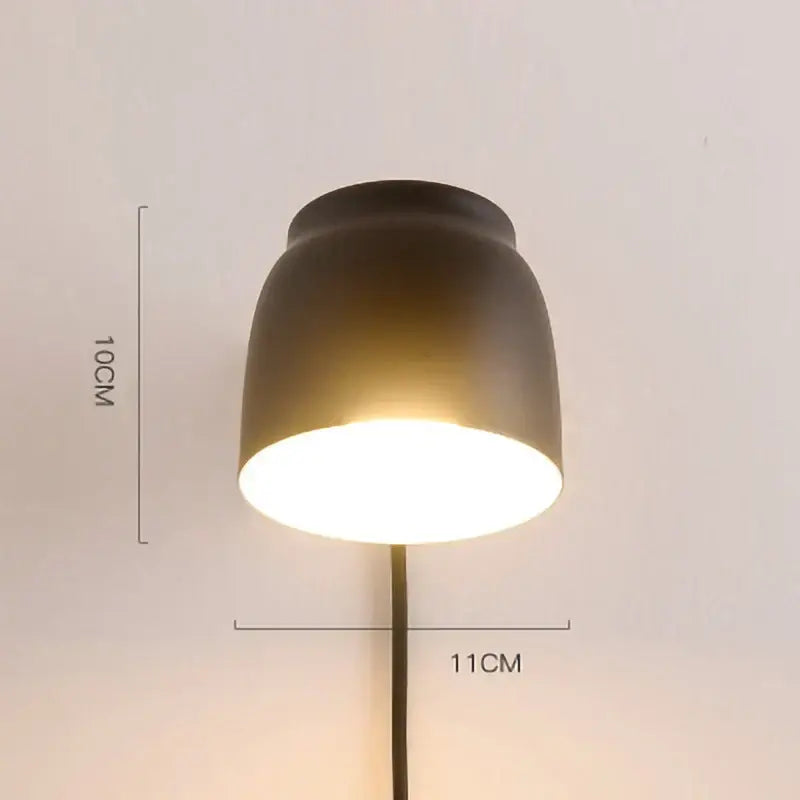 Modern ceramic and wood led wall lamp with a matte black ceramic lampshade emitting warm reading light glow