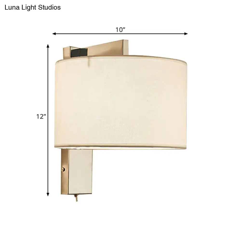 A sleek modern wall sconce with an off-white fabric drum shade and brushed brass frame in white black tones