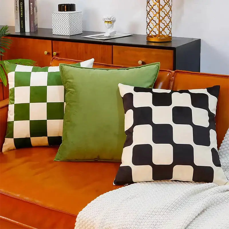 Three modern checkered decorbites fluffy velvet cushion covers in green black and white on an orange couch