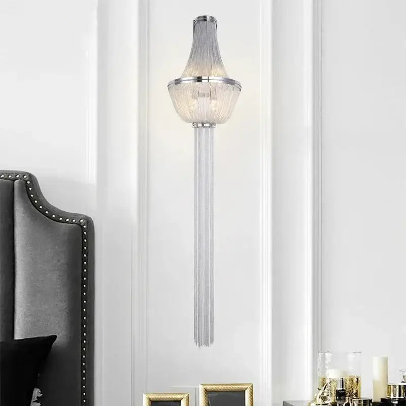 A modern chrome aluminum chain sconce featuring cascading glass prisms for bedroom wall lighting