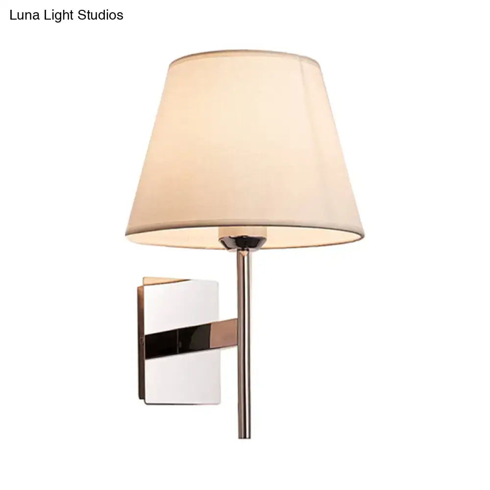 Modern wall light featuring a chrome-finished metal arm and cream fabric cone shade for bedroom use