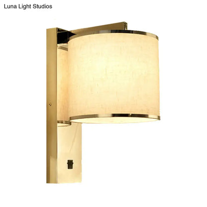 Gold-finished living room wall sconce with cylindrical off-white fabric shade and metallic rims in modern chrome style
