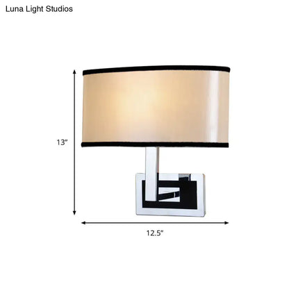Modern chrome and beige oval wall sconce with cylindrical lampshade and black trim for bedroom lighting