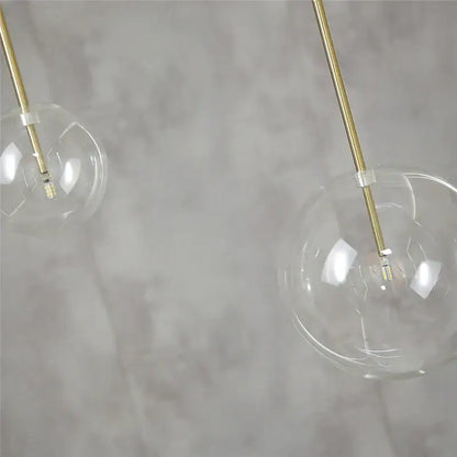 Modern chrome and brass pendant light with clear glass globe and slender brass rods for kitchen lighting