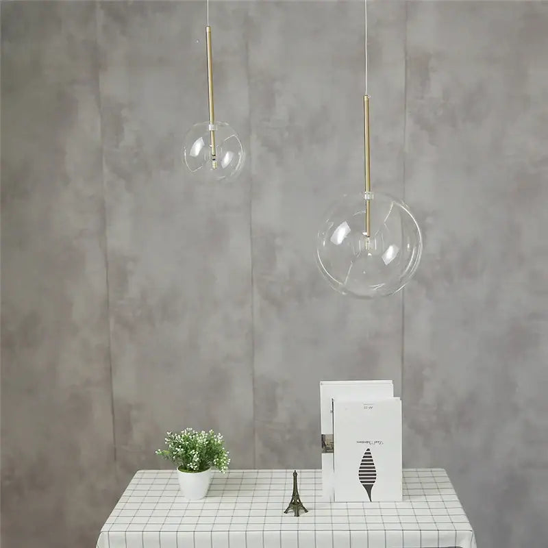 Two clear glass globe pendant lights with gold-toned rods in modern chrome and brass kitchen pendant light design