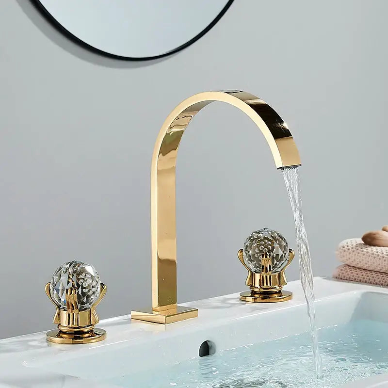 Modern chrome arched dual handle basin faucet with gold finish crystal globe handles and water flowing from the spout