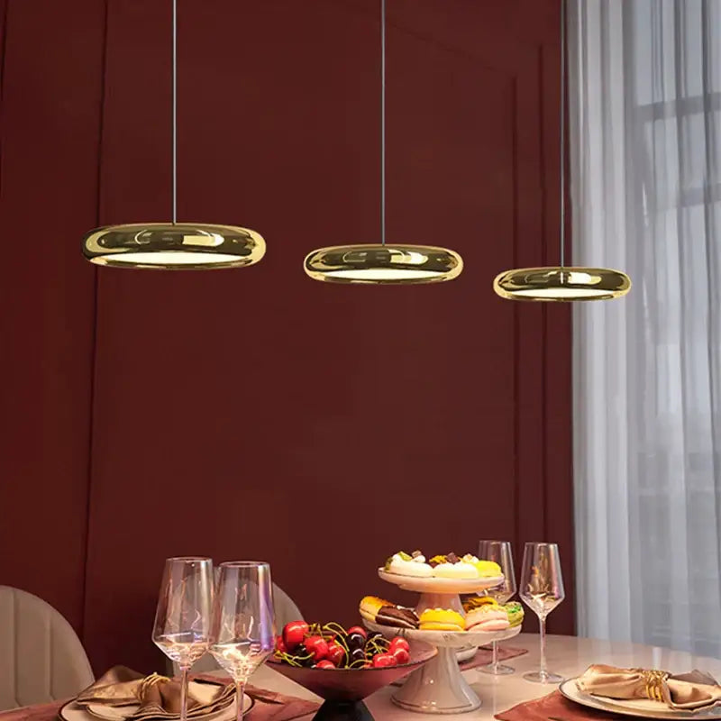Three sleek gold-finished decorbites circular dining pendant led lights hang above a modern dining table