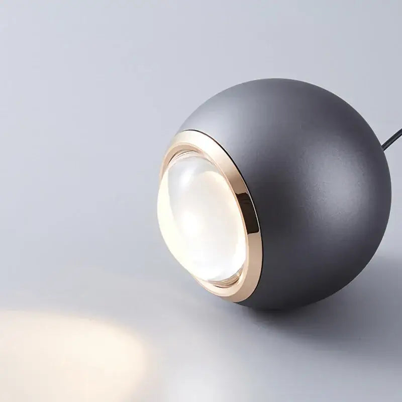 Matte black spherical ball pendant light with gold-toned rim and clear glass lens for modern dining room lighting