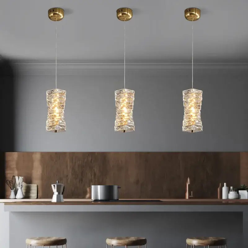 Three elegant gold-finished decorbites crystal dining pendant lamps with textured glass shades above kitchen island