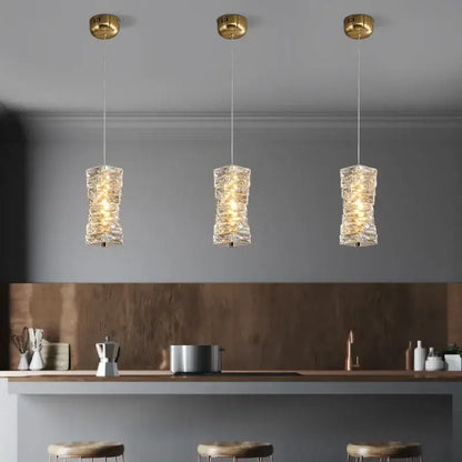 Three elegant gold finished crystal led pendant lights with textured glass shades hang above a modern kitchen counter