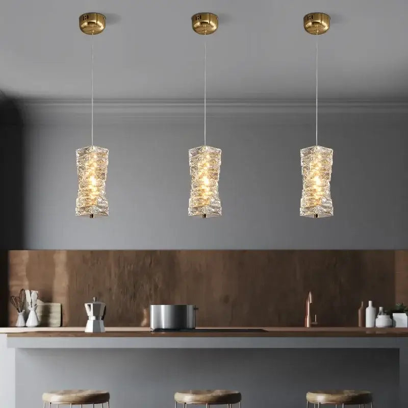 Three elegant gold finished crystal led pendant lights with textured glass shades hang above a modern kitchen counter