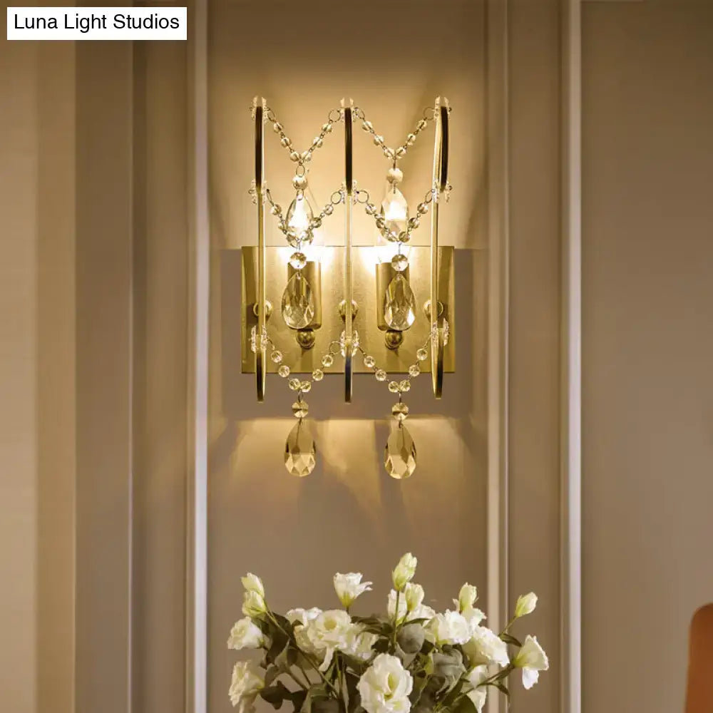 Gold-toned crystal wall sconce light type with dangling teardrop crystals for modern bedroom lighting