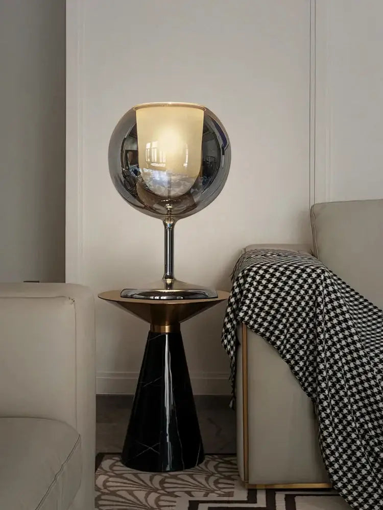A sleek spherical chrome glass gold table lamp with warm glow on black marble pedestal for luxury living room decorbites table lamp